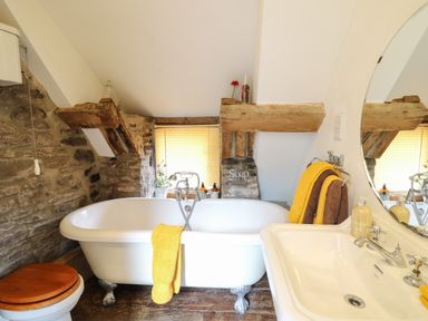 A bathroom with a clawfoot bathtub towels and a sink with a round mirror at Ty Fferm Hen in Talybont-on-Usk