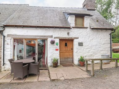 A white stone cottage with a wooden door and patio furniture outside at Ty Fferm Hen in Talybont-on-Usk