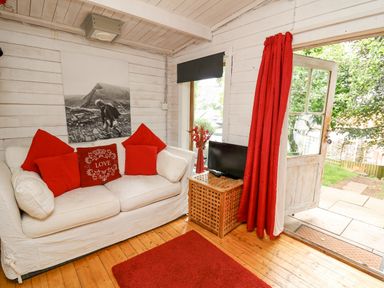 A living room with a white sofa with red pillows a small wooden table with a television and red curtains at Ty Bach Twt in Talybont-on-Usk