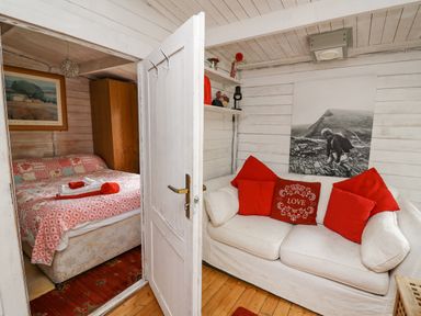 A small living area with a white sofa and red pillows next to a bedroom with a bed covered in patterned bedding at Ty Bach Twt in Talybont-on-Usk