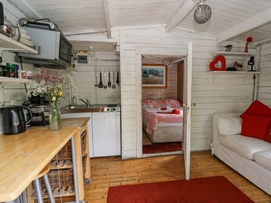 A small kitchen area with wooden counter and utensils next to a doorway leading to a bedroom with a bed covered in a patterned quilt at Ty Bach Twt in Talybont-on-Usk