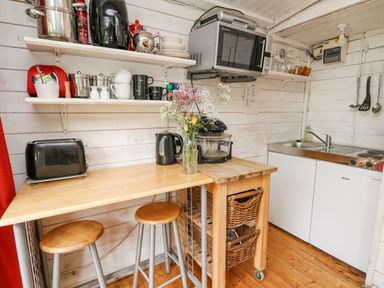 A kitchen with wooden stools a toaster a microwave and kitchen utensils at Ty Bach Twt in Talybont-on-Usk