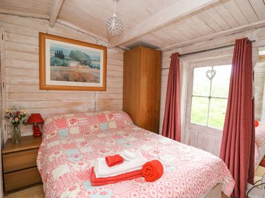 A bedroom with a patterned bedspread on a bed next to a wooden wardrobe and window with red curtains at Ty Bach Twt in Talybont-on-Usk
