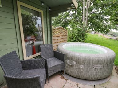 An outdoor patio area with two woven chairs and an inflatable hot tub near a green building with a window at Ty Bach Twt in Talybont-on-Usk