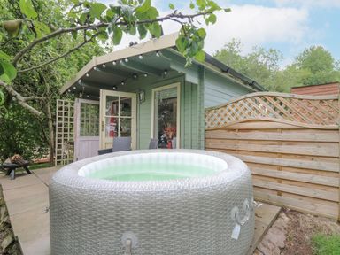 An outdoor patio area with an inflatable hot tub chairs a small green cabin and a wooden privacy fence at Ty Bach Twt in Talybont-on-Usk