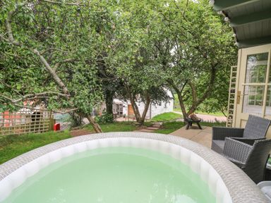 An outdoor area with a circular hot tub a patio with two chairs a fire pit and trees at Ty Bach Twt in Talybont-on-Usk