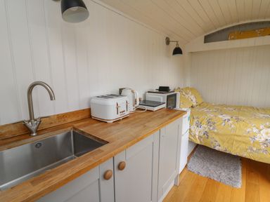 A kitchenette with a sink toaster kettle microwave and induction cooker next to a bed with yellow floral bedding at Ty Olwyn Bach in Talybont-on-Usk