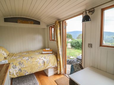 A small bedroom with a single bed and a desk near windows and an open door showing an outdoor view at Ty Olwyn Bach in Talybont-on-Usk