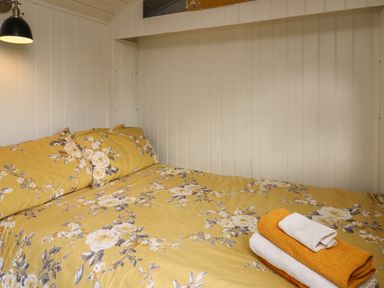 A bed with yellow floral bedding and folded towels on it in a wooden paneled room at Ty Olwyn Bach in Talybont-on-Usk