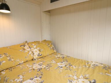 A bed with yellow floral bedding against white paneled walls with a black wall lamp at Ty Olwyn Bach in Talybont-on-Usk