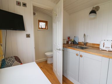 A small kitchen area with a sink and toaster next to an open door showing a toilet inside a small bathroom at Ty Olwyn Bach in Talybont-on-Usk