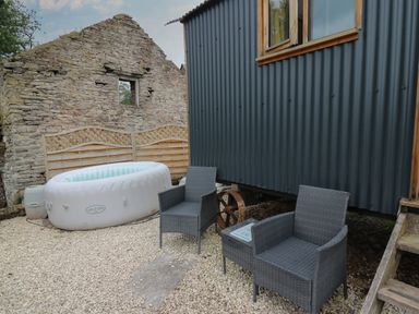 An outdoor seating area with two gray chairs next to an inflatable Lay-Z-Spa outside a corrugated metal building at Ty Olwyn Bach in Talybont-on-Usk