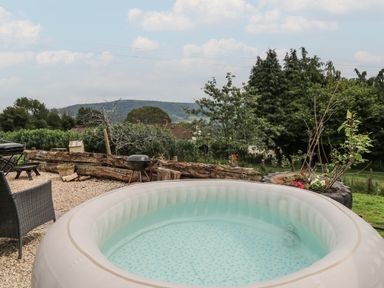 An outdoor area with an inflatable hot tub a charcoal grill garden planters trees and mountains in the background at Ty Olwyn Bach in Talybont-on-Usk