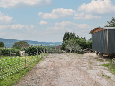 An outdoor area with a metal fenced enclosure a shed tire planter and barbecue with hills in the background at Ty Olwyn Bach Talybont-on-Usk