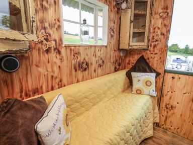 A small sitting area with a yellow quilted couch and floral pillows in a wooden room with butterfly designs at Ty Gwenyn in Talybont-On-Usk