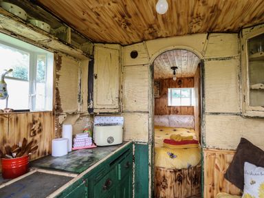 A small kitchen area with burnt wood cabinets and a view into a bedroom with a yellow bee patterned bedspread at Ty Gwenyn in Talybont-On-Usk