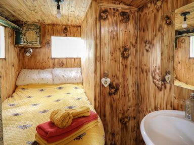 A small wooden bedroom with a bed covered in a yellow bee patterned blanket and folded towels next to a white sink with a mirror at Ty Gwenyn in Talybont-On-Usk