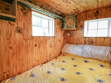 A wooden bedroom with windows and a bed covered with a yellow blanket with bee patterns at Ty Gwenyn in Talybont-On-Usk