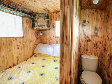 A small wooden room with a bed covered with a yellow bee-patterned blanket and a white pillow next to a toilet at Ty Gwenyn in Talybont-On-Usk