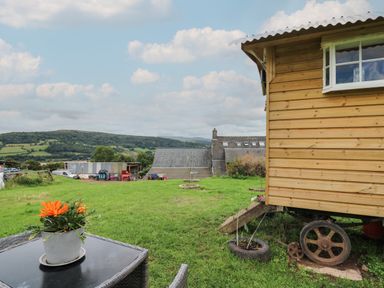 A garden with green grass a wooden wagon and flowers on a table at Ty Gwenyn in Talybont-On-Usk