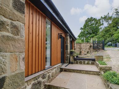 An exterior view of a stone and wood building with steps leading to a black door and a small garden space at The Bothy Riding Hills in Riding Mill near Corbridge