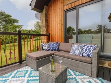 An outdoor seating area with a gray wicker sofa and blue patterned cushions on a deck with wooden railing at The Bothy Riding Hills Riding Mill near Corbridge