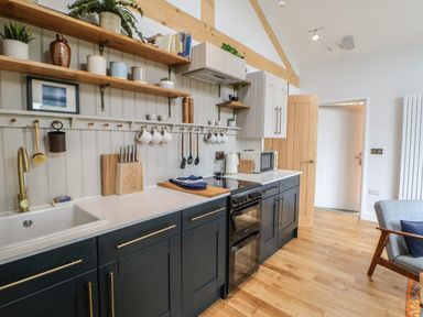 A kitchen with black lower cabinets wooden open shelves and a white countertop at The Bothy Riding Hills in Riding Mill near Corbridge