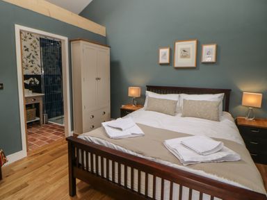 A bedroom with a wooden bed and beige bedding with a wardrobe and two bedside tables with lamps at The Bothy Riding Hills in Riding Mill near Corbridge