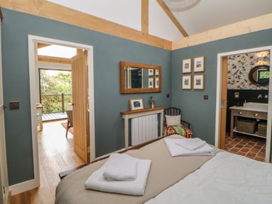 A bedroom with bed towels a chair a mirror and two doorways one leading to a balcony the other to a bathroom at The Bothy Riding Hills in Riding Mill near Corbridge