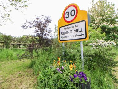 A road sign saying welcome to Riding Mill with flowers and greenery surrounding it at The Bothy Riding Hills in Riding Mill near Corbridge