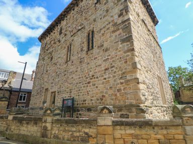 A large stone building with small windows and a sign outside surrounded by a low stone wall