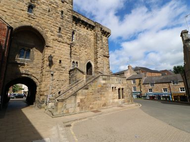 A stone building with an arched entrance and stairs beside a street with shops in the background