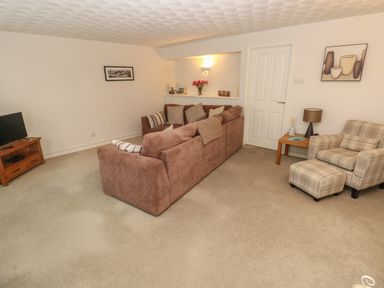 A living room with brown sofa and plaid armchair with ottoman at Flat 1 in Tenby
