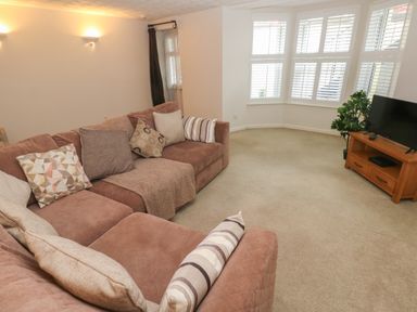 A living room with a brown sectional sofa with cushions a wooden TV stand with a TV and a plant near bay windows at Flat 1 in Tenby