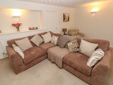 A living room with a brown sofa with cushions a beige armchair a lamp wall lights paintings and flowers on a shelf at Flat 1 in Tenby