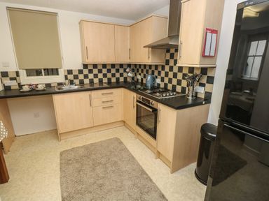 A kitchen with light wood cabinets black countertops a stainless steel stove a sink a window with a blind a black refrigerator and a brown rug on the floor at Flat 1 in Tenby