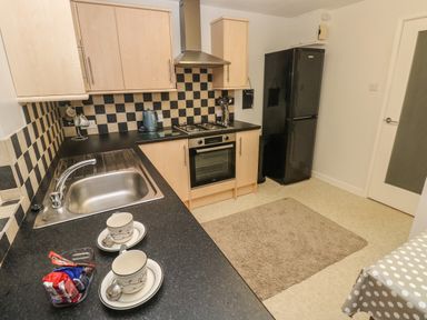 A kitchen with a sink stove oven fridge and two cups on a counter at Flat 1 in Tenby