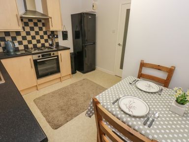 A kitchen with wooden cabinets a black refrigerator a table set for two with plates and cutlery at Flat 1 in Tenby