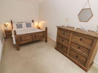 A bedroom with a wooden bed and matching dresser against light walls at Flat 1 in Tenby
