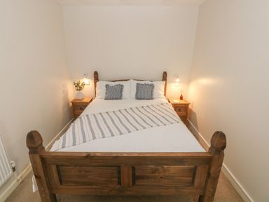 A bedroom with a wooden bed and two bedside tables with lamps and decorations at Flat 1 in Tenby