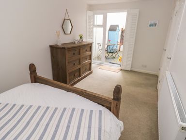 A bedroom with wooden bed and dresser and glass door leading to outdoor seating at Flat 1 in Tenby
