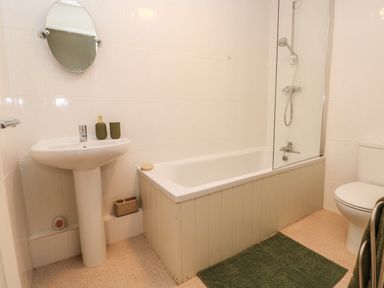 A bathroom with a sink mirror bathtub shower toilet and green bath mat at Flat 1 in Tenby