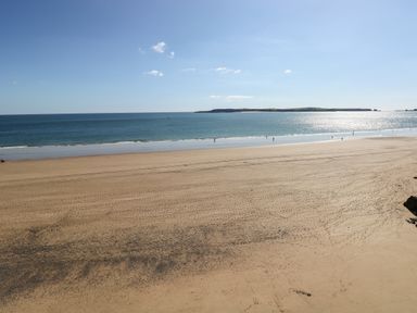 A sandy beach with people near the water and an island in the distance at Flat 1 in Tenby