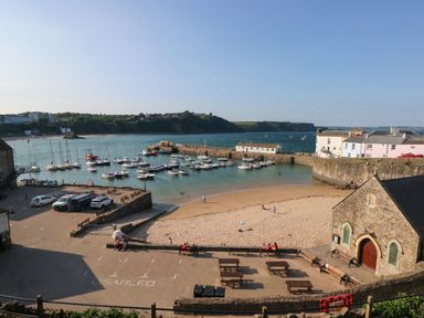 A harbor with boats docked near a sandy beach and stone buildings at Flat 1 in Tenby