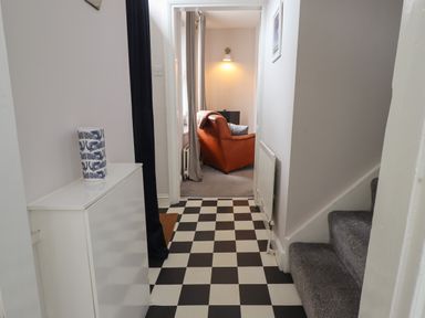 A hallway with black and white checkered floor leading to a room with an orange armchair and a gray carpet at White Feathers in Alnwick