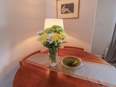 A wooden dining table with a floral centerpiece bowl and table runner with chairs and a framed artwork on the wall at White Feathers in Alnwick