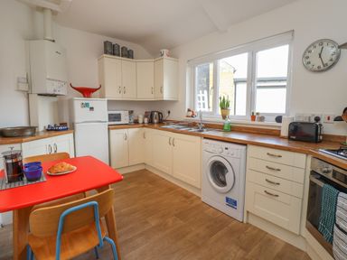 A kitchen with white cabinets a red table with chairs a washing machine and a window at White Feathers in Alnwick