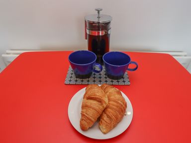 Two croissants on a white plate with a French press and two blue cups on a red table at White Feathers in Alnwick