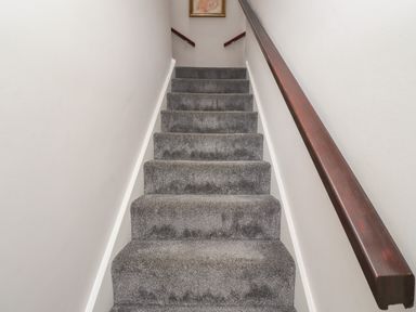 A carpeted staircase with grey steps and dark wooden handrail on the right at White Feathers in Alnwick