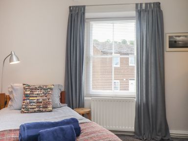 A bedroom with a bed a lamp a window with curtains and a small stool at White Feathers in Alnwick